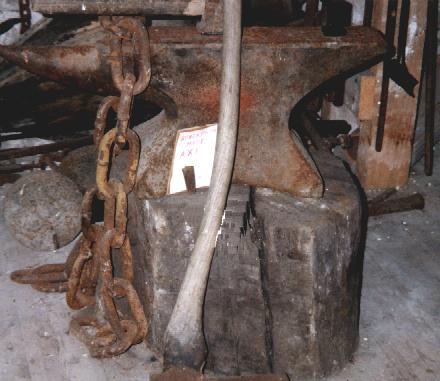 Reuben's anvil is draped with a thick chain and a large axe leans against the side of it.